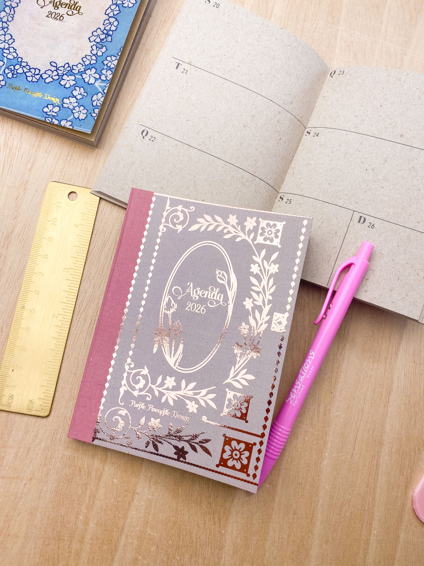 DuAS agendas 2026, régua dourada e caneta rosa numa mesa de madeira clara