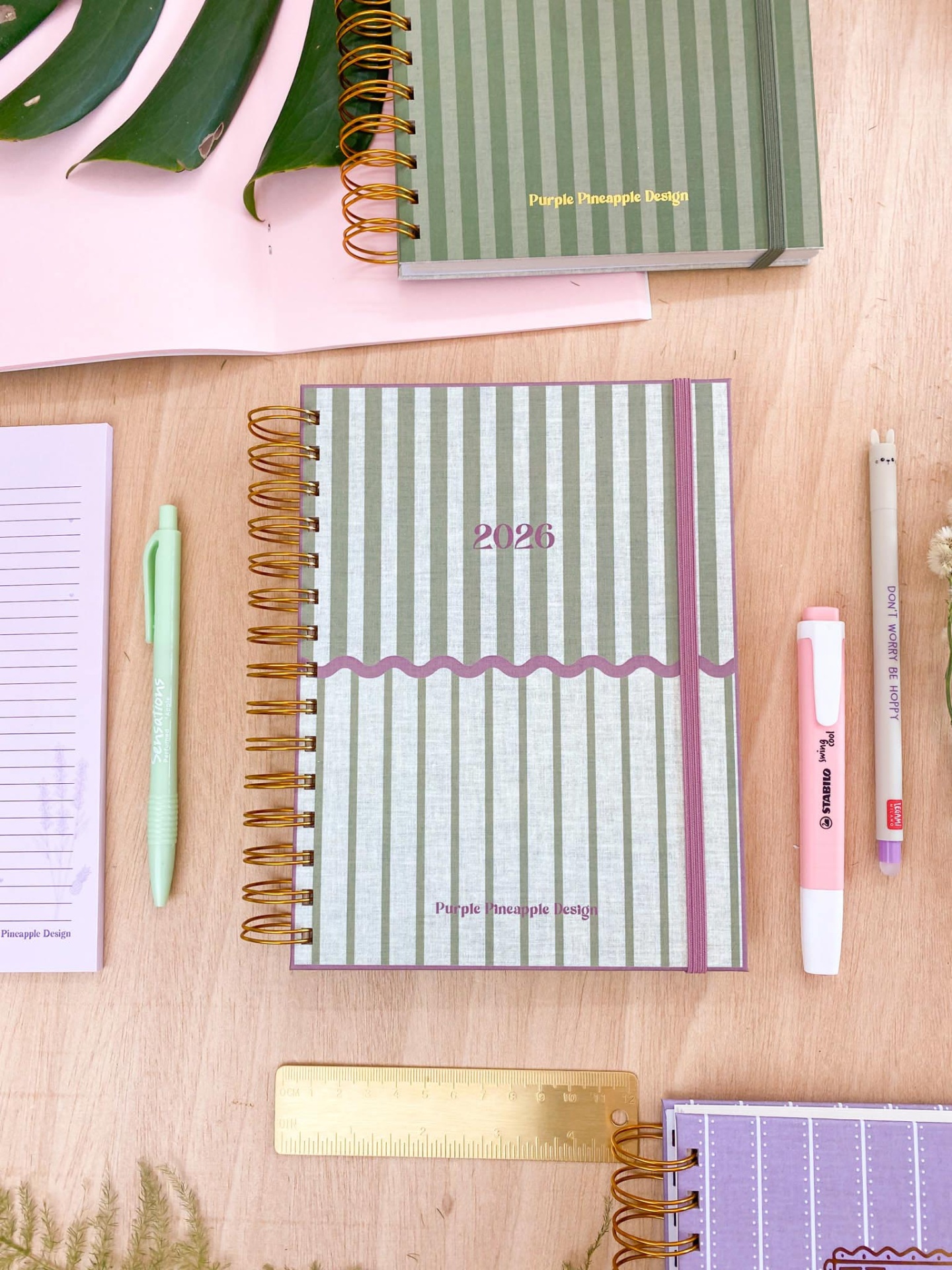 Caderno com capa riscada verde e branca e canetas coloridas sobre mesa de madeira