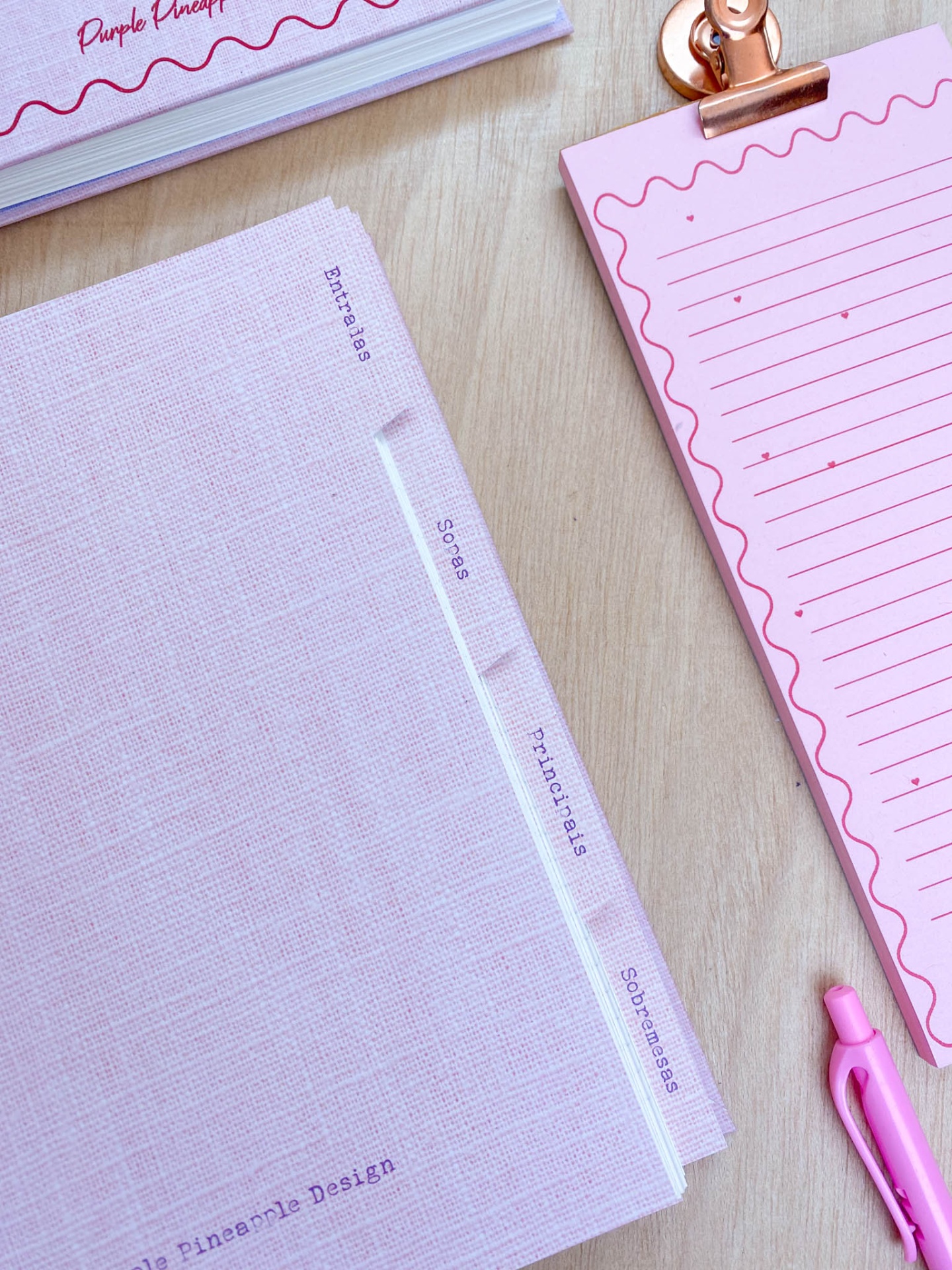 Pasta de arquivo cor-de-rosa com divisórias, bloco de notas cor-de-rosa e caneta rosa sobre secretária de madeira