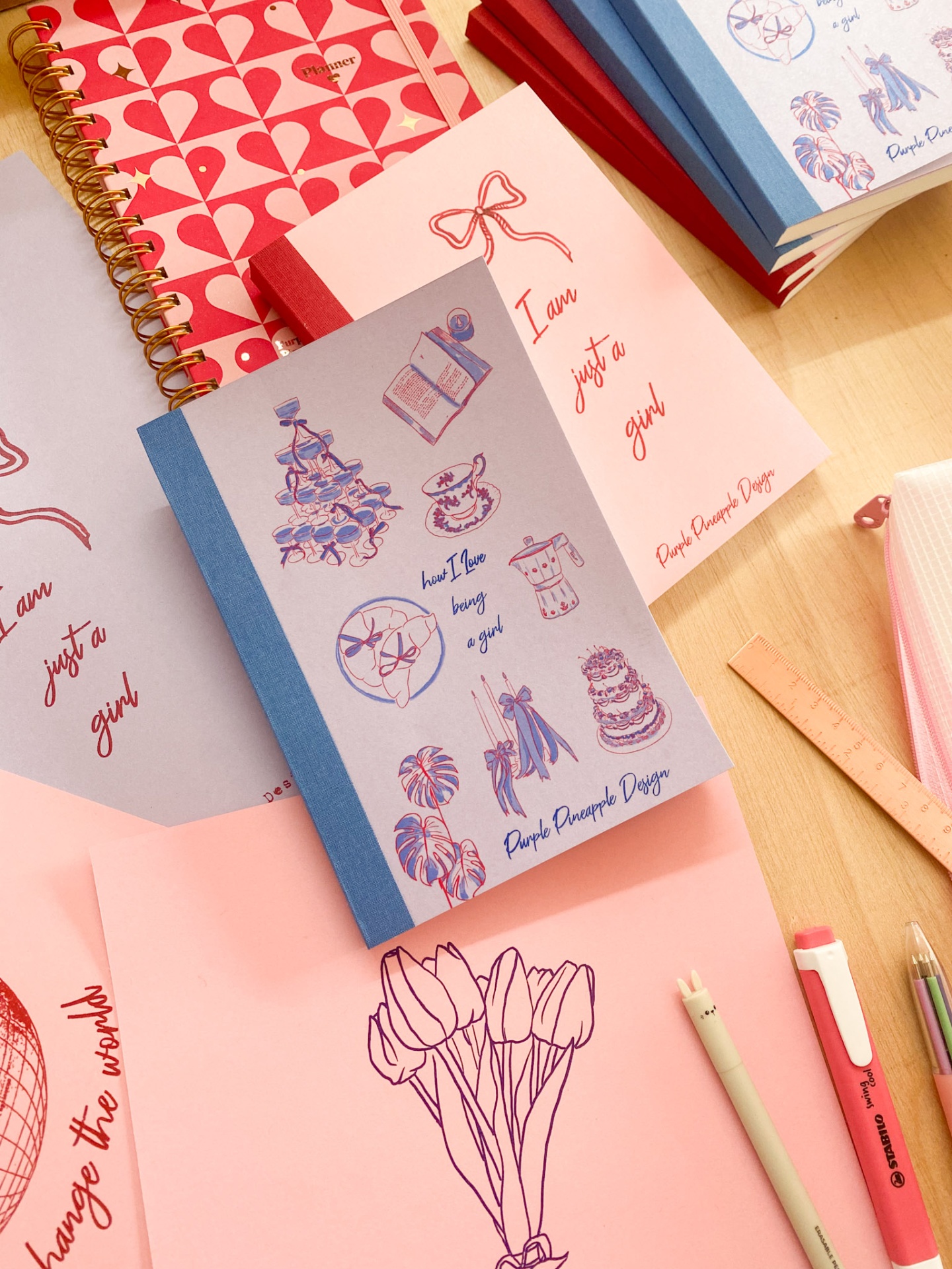 🖌️ As melhores inspirações de capas para bullet journal Cadernos e blocos de notas coloridos com ilustrações e texto, sobre superfície de madeira com canetas ao lado.