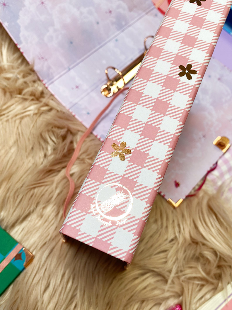 Caixa rosa quadriculada com flores douradas sobre superfície felpuda