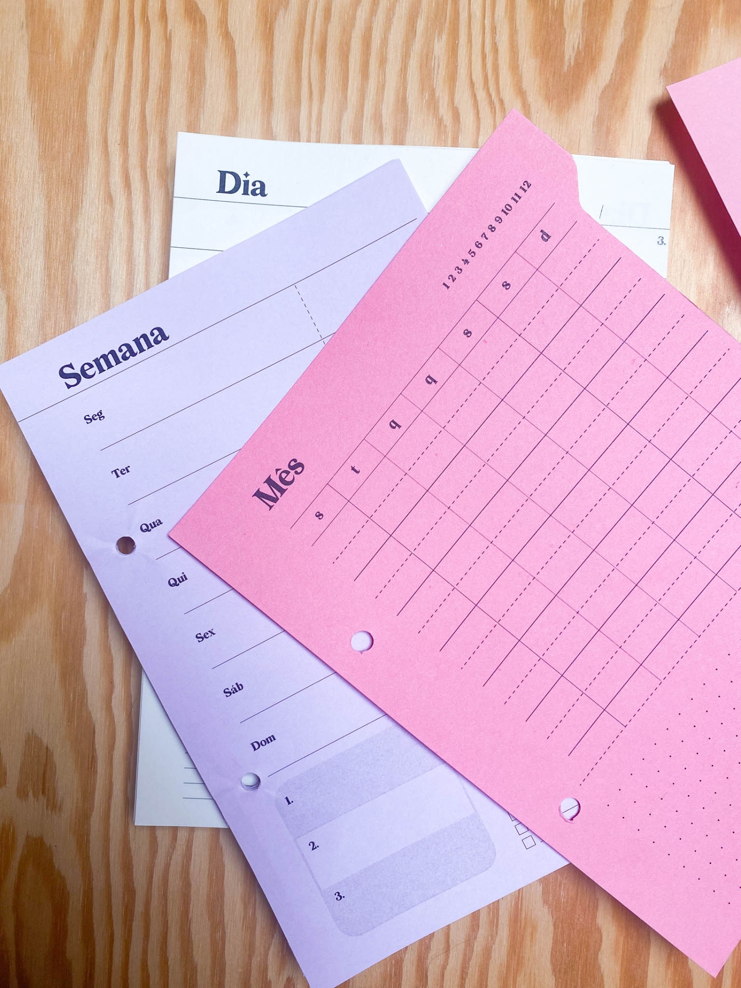 Folhas de calendário em tons pastel sobre mesa de madeira clara.