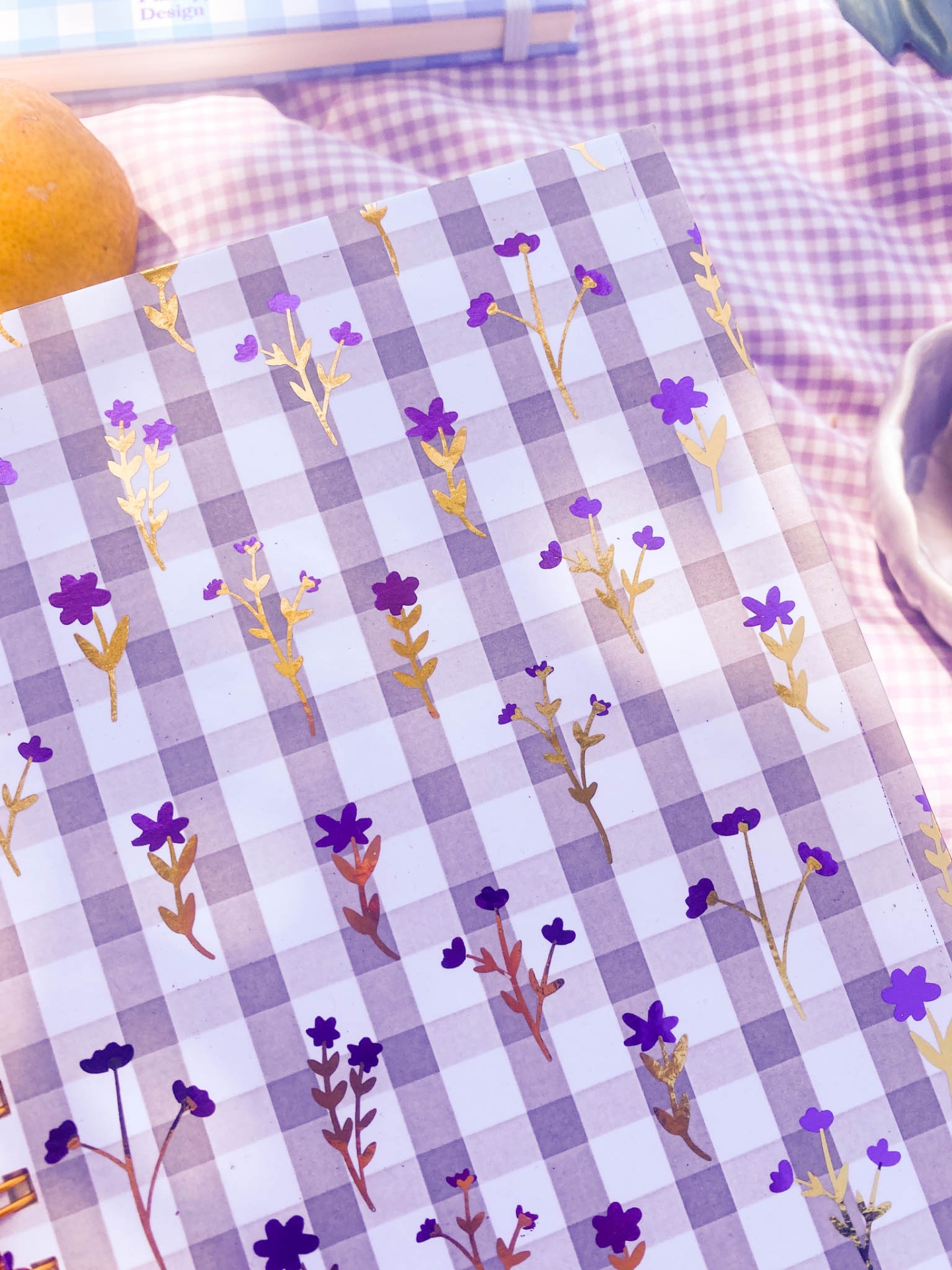 Papel de embrulho xadrez com flores roxas e douradas sobre tecido xadrez roxo