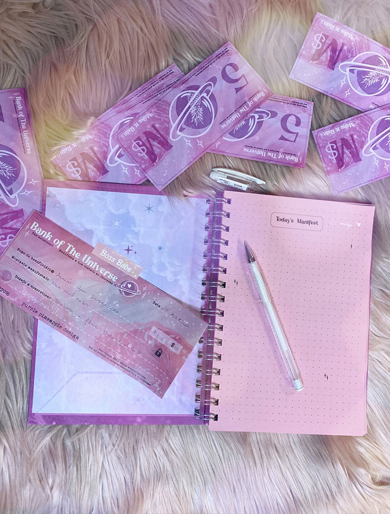 Caderno rosa aberto com caneta e cartões lilases sobre tapete felpudo rosa