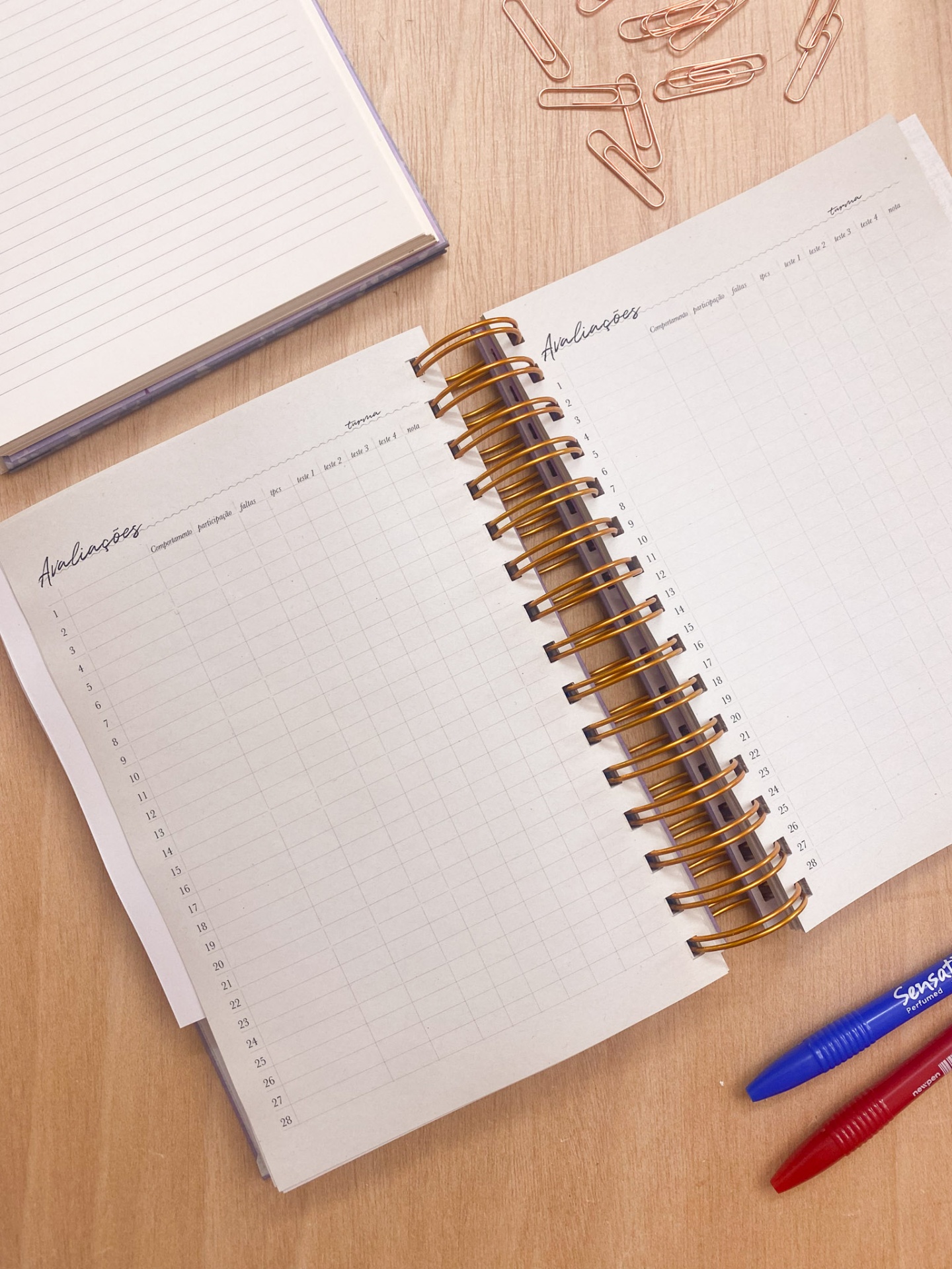 Agenda espiral aberta com canetas e clipes sobre mesa de madeira
