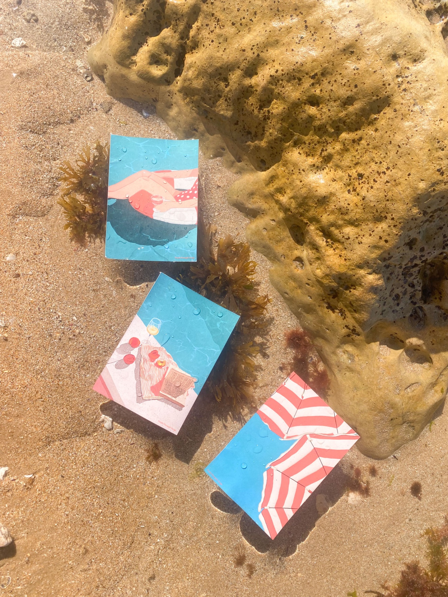 Telemóveis com capas coloridas junto a uma rocha na areia da praia molhada