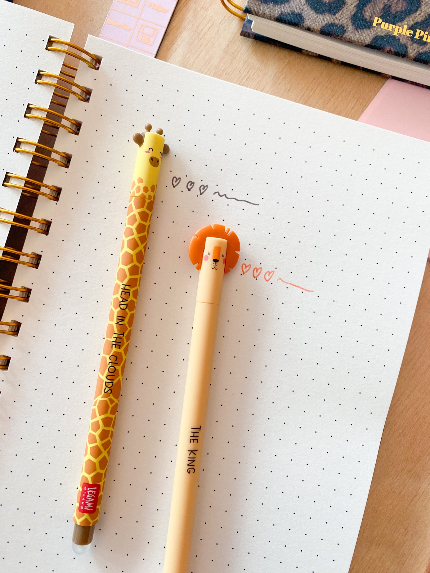 Dois lápis temáticos - girafa e leão - sobre caderno pontilhado.