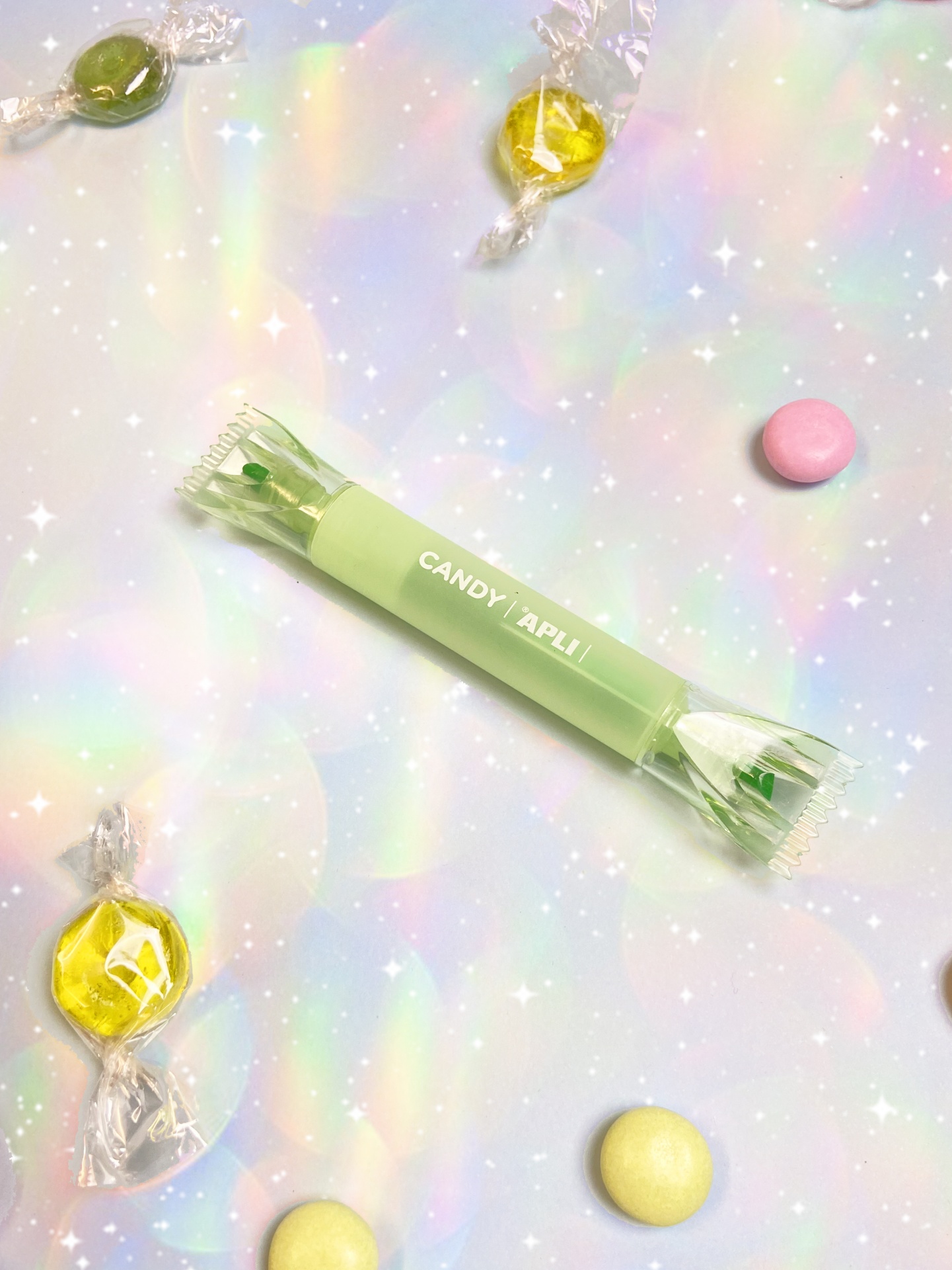 Pacote de doce verde claro com texto CANDY APLI e doces coloridos num fundo iridescente brilhante