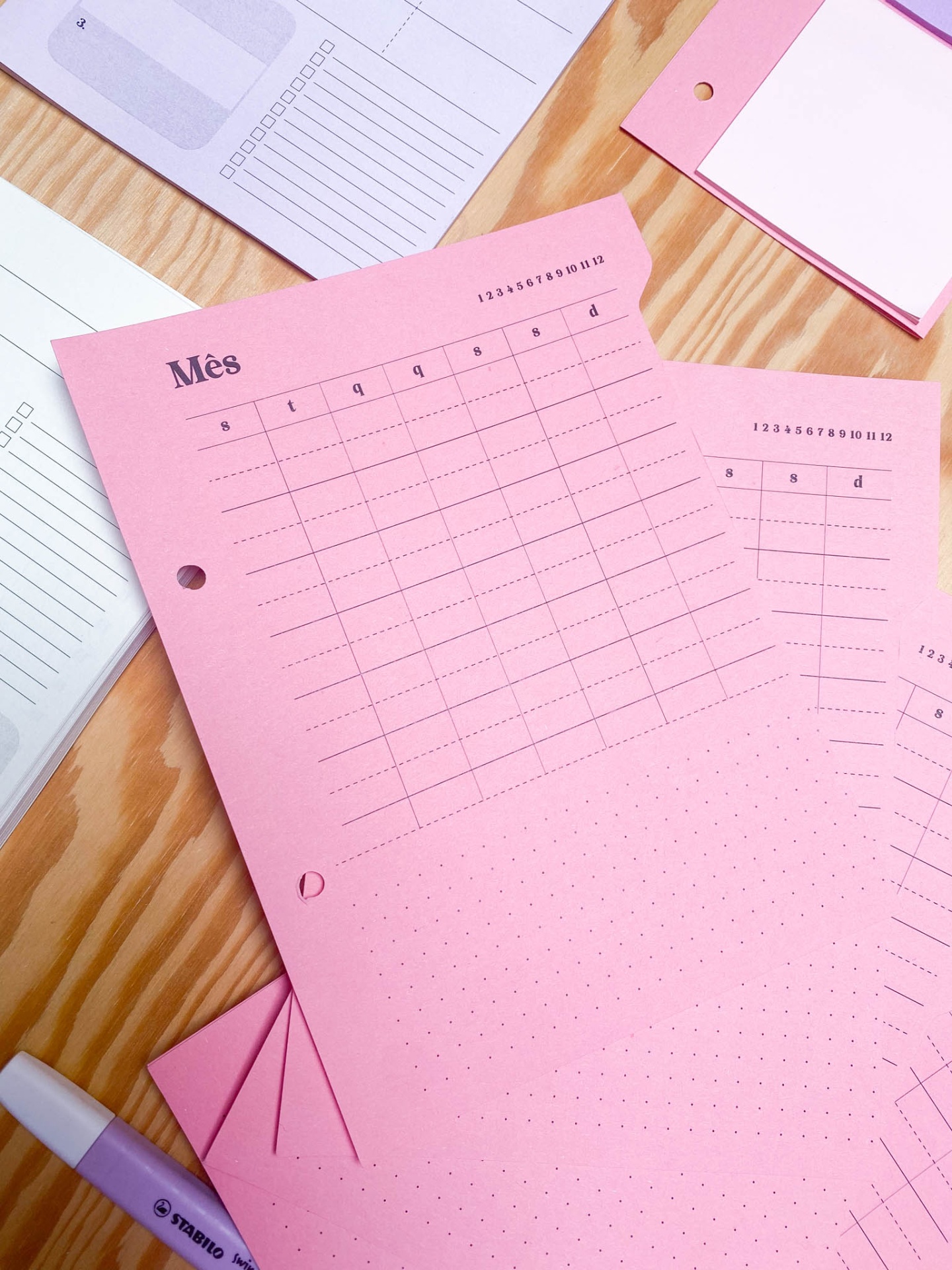 Folhas cor-de-rosa com calendário mensal impresso sobre mesa de madeira ao lado de marcador Stabilo lavanda