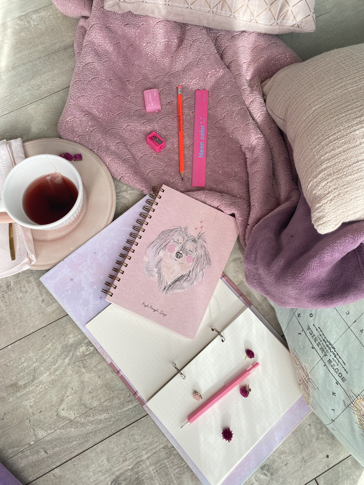  Espaço aconchegante com chá, cadernetas ilustradas, material de escrita rosa-laranja e manta cor de rosa