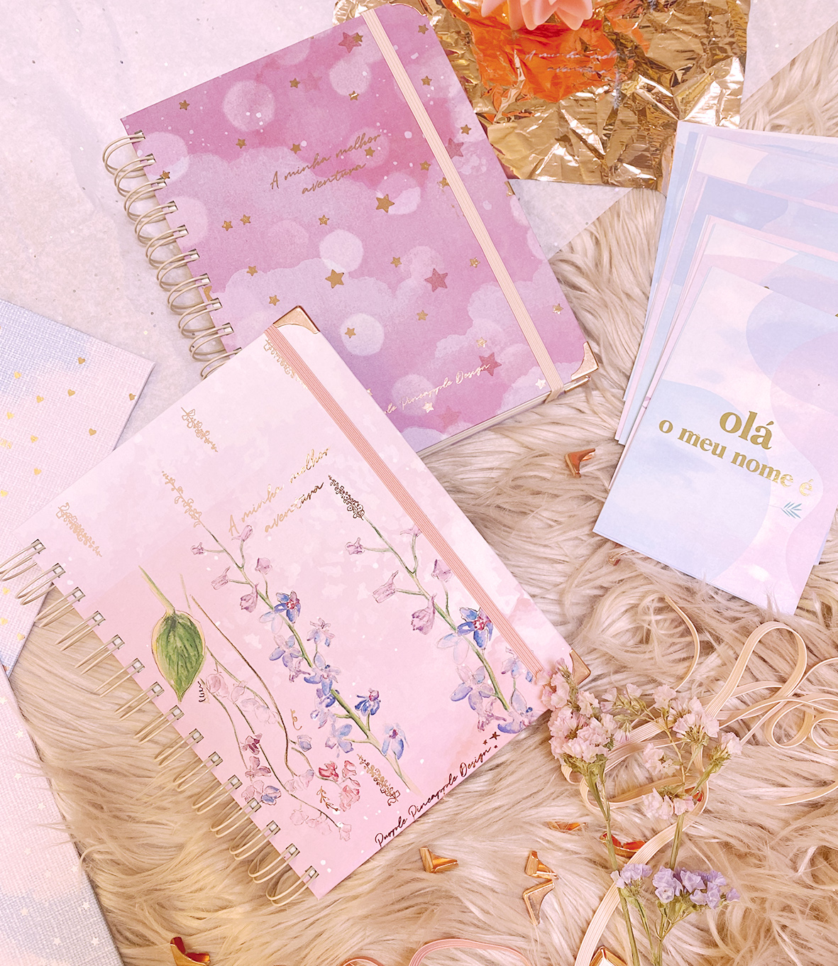 Dois cadernos em espiral decorados sobre superfície felpuda com papéis azuis e flores secas