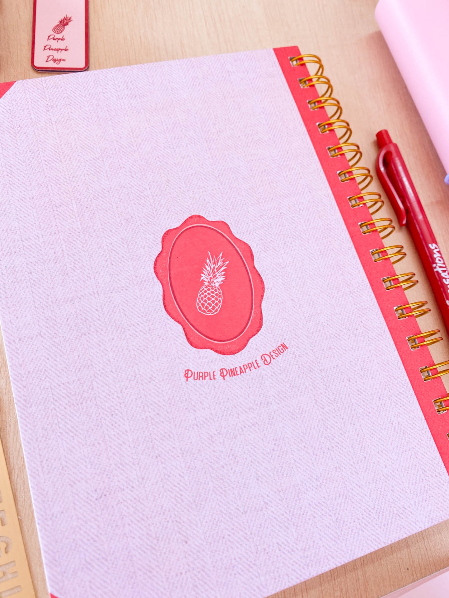 Caderno rosa com lombada vermelha e logótipo de abacaxi vermelho