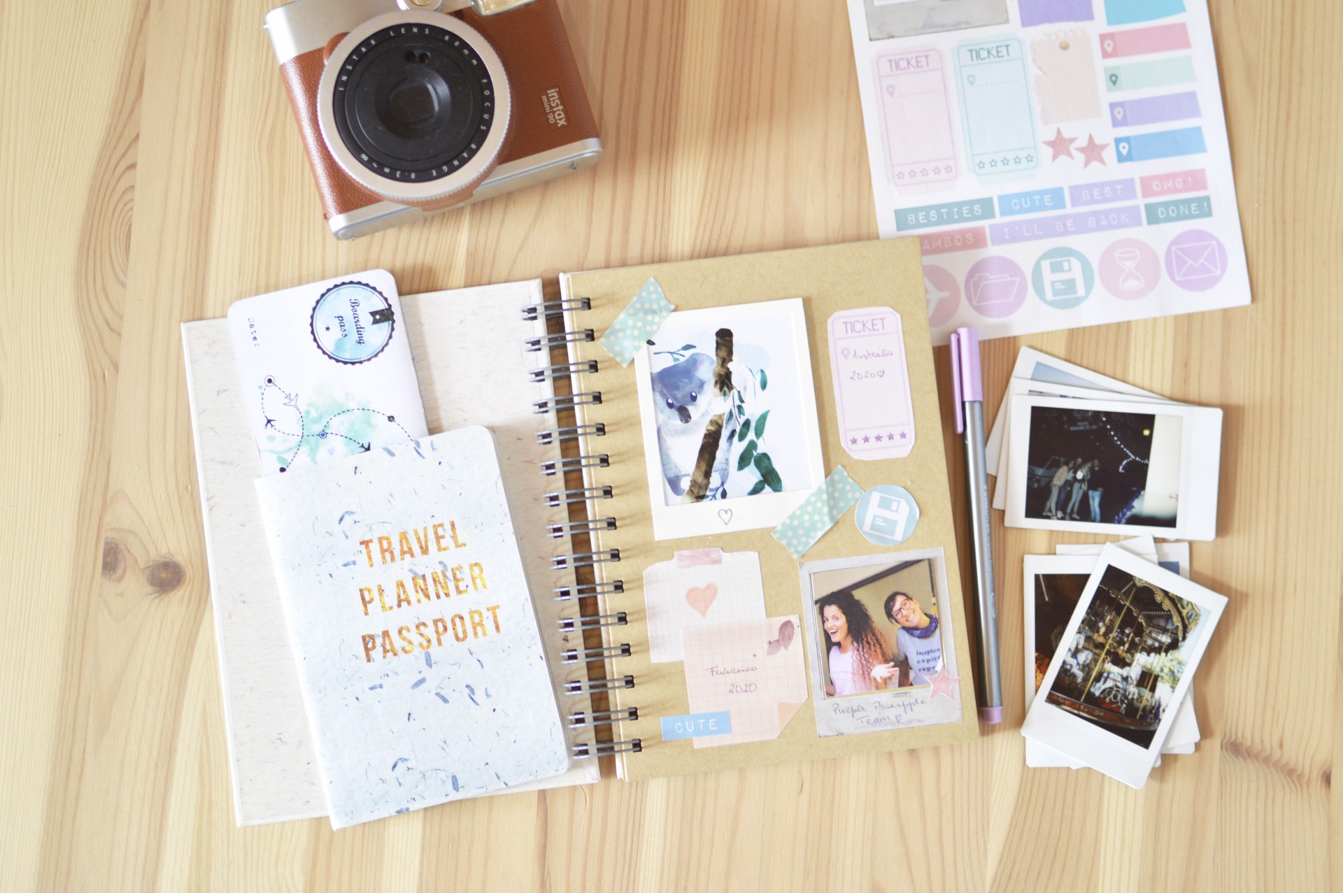 caderno de planner de viagem com fotos, autocolantes, fotos Polaroid e câmara instantânea numa mesa de madeira clara
