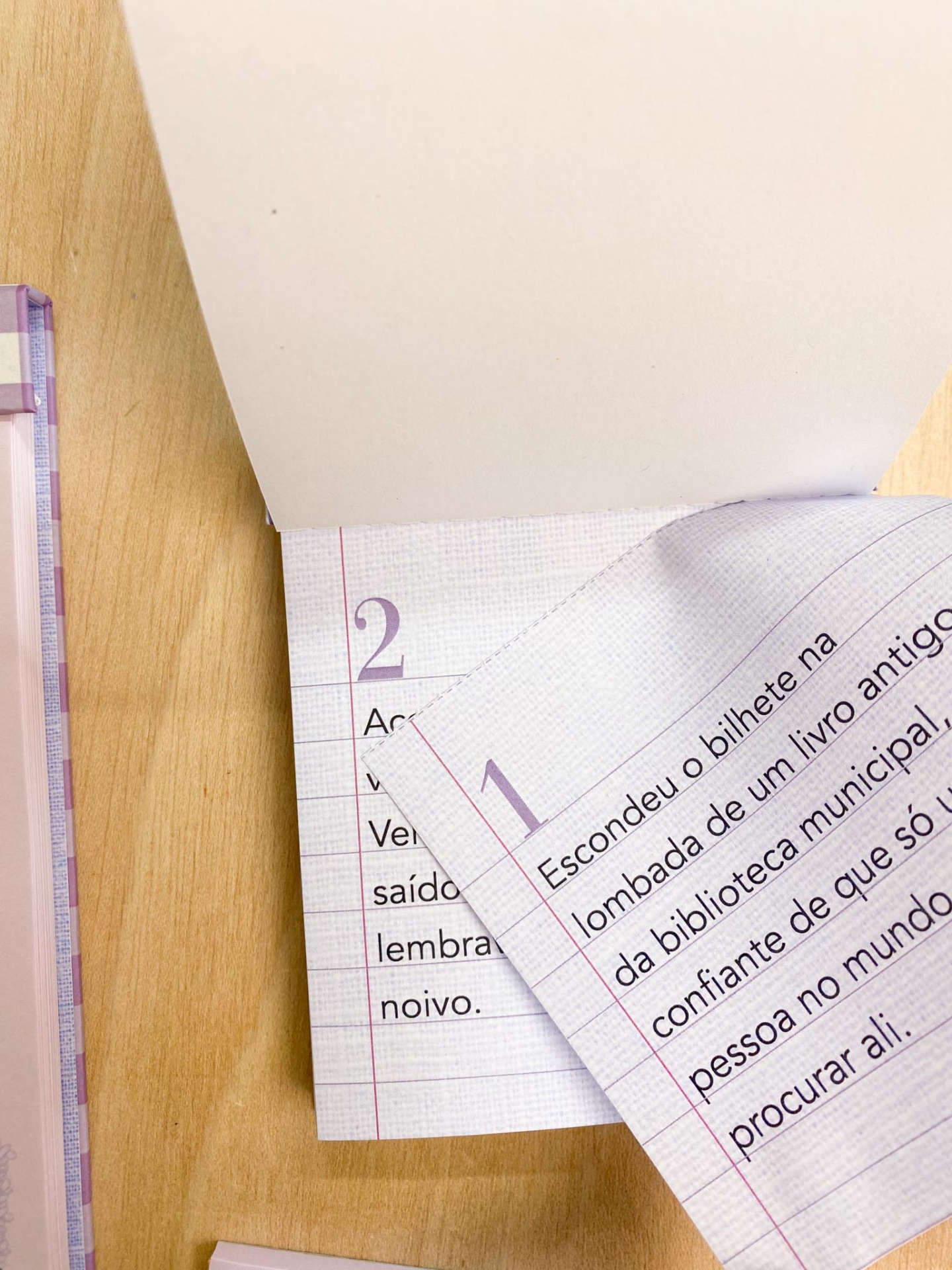 Caderno de papel quadriculado com texto em português sobre superfície de madeira clara