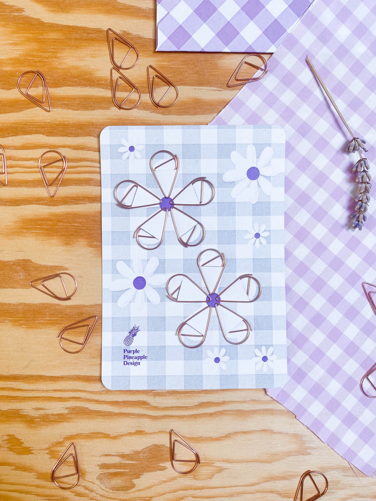 Clips de metal em forma de pétalas sobre cartão decorativo e pano xadrez lilás
