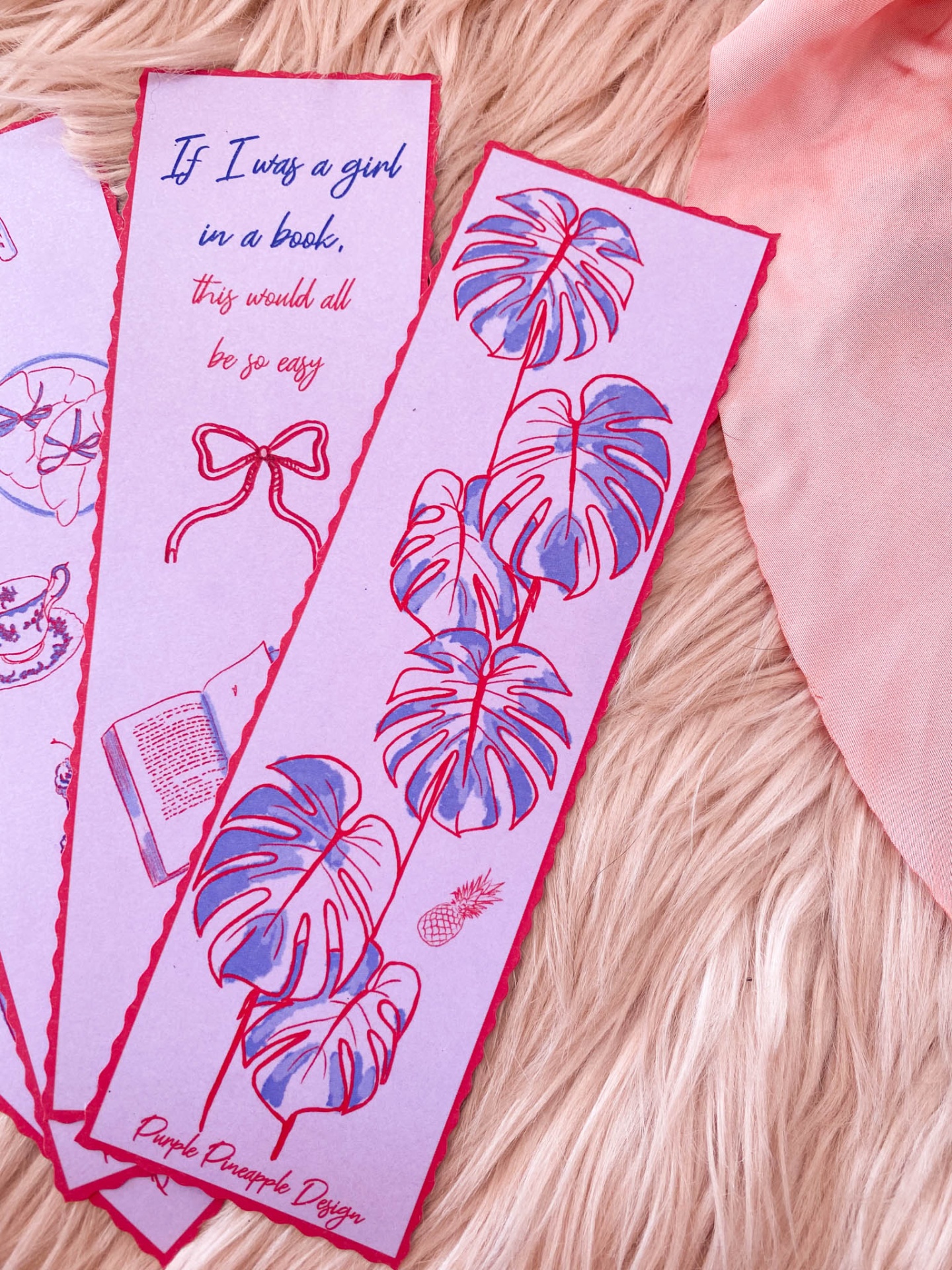 Marcadores de livros cor de rosa com desenhos de folhas e texto sobre superfície felpuda creme e tecido rosa.