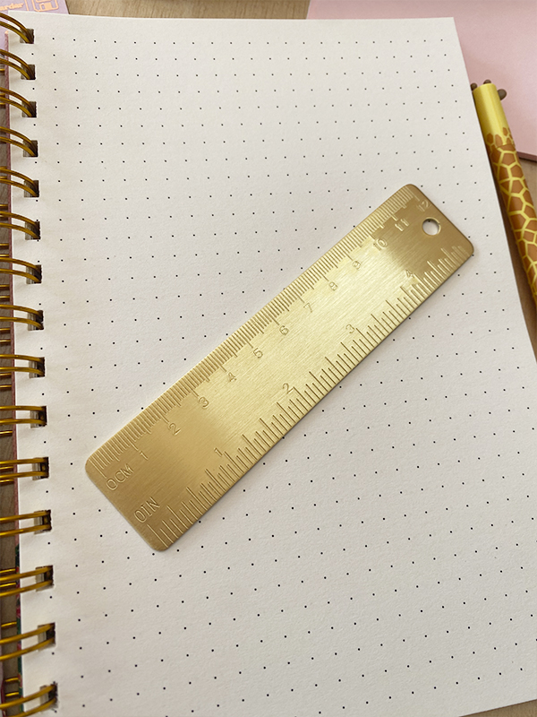 Caderno com folhas pontilhadas, régua metálica dourada e caneta com padrão de girafa
