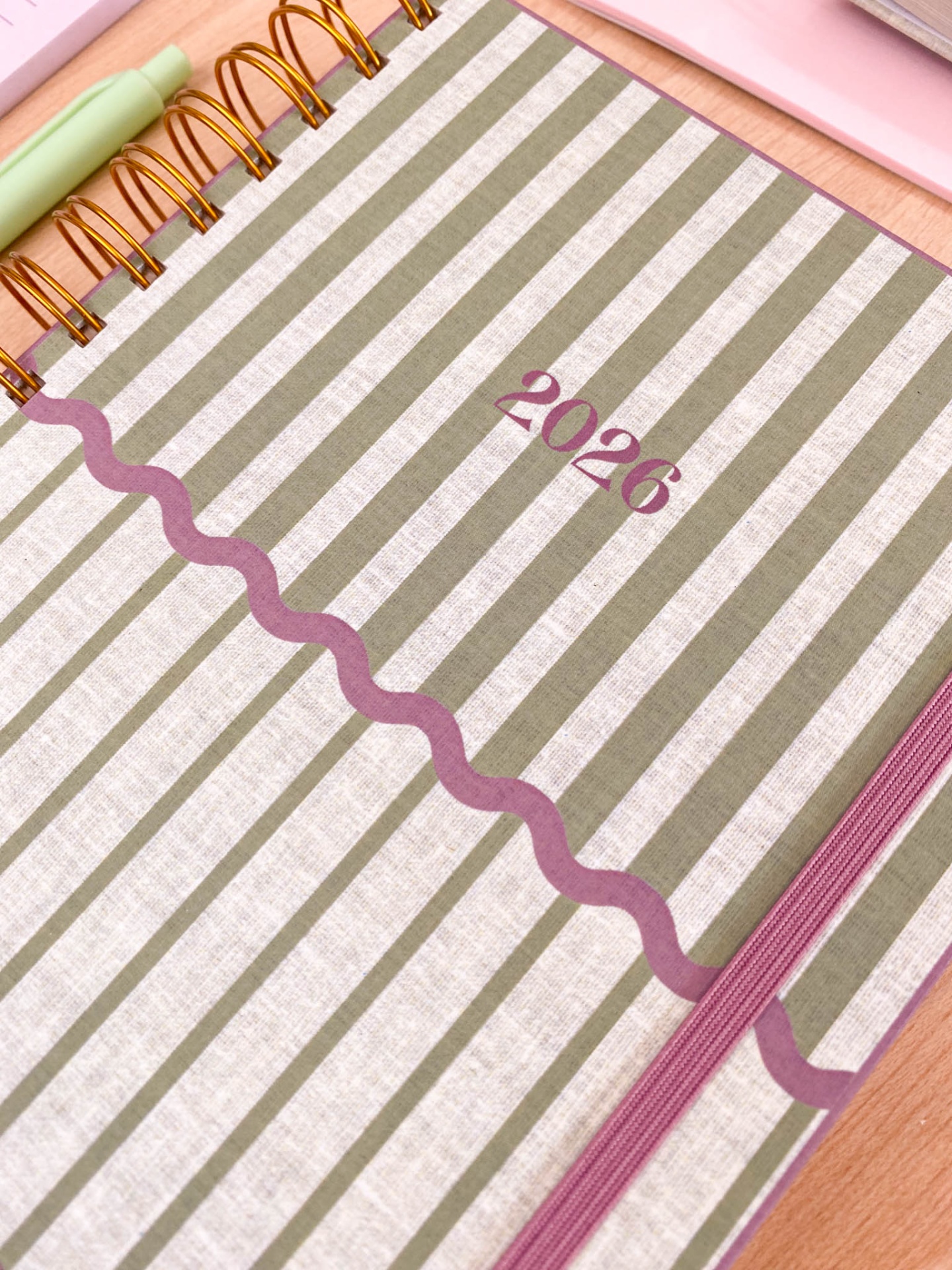 Agenda 2026 com capa riscada verde e bege, elástico rosa, vista lateral