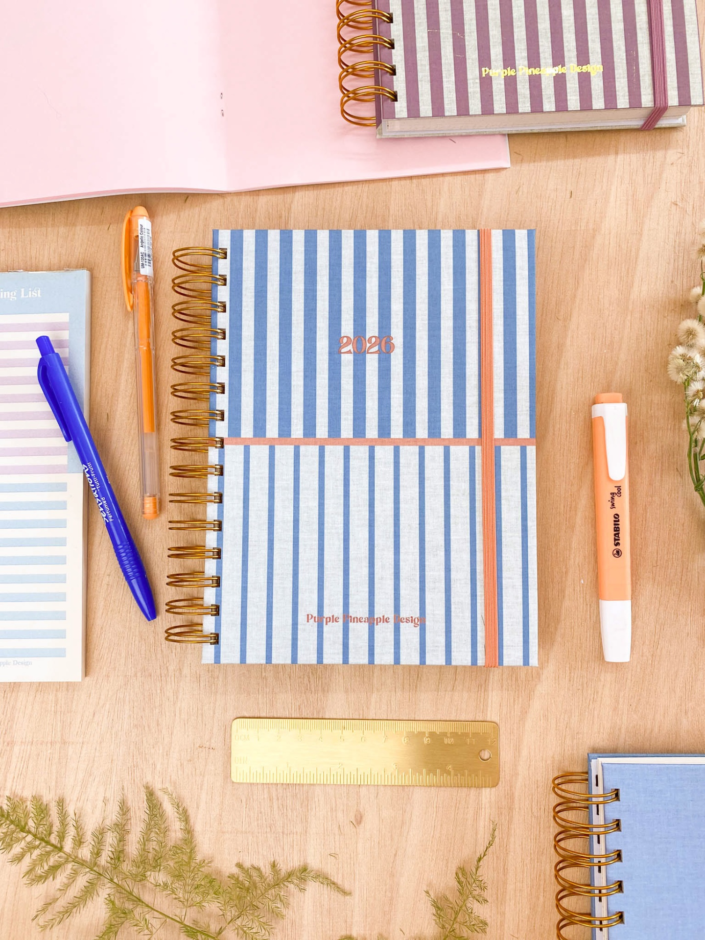 Caderno espiral riscado azul branco com canetas e régua dourada em mesa de madeira