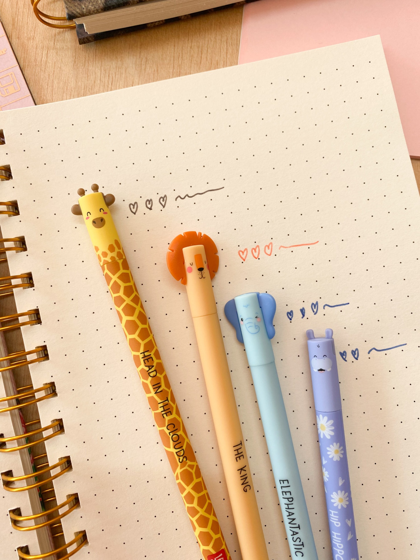 Quatro canetas com designs de animais sobre folha pontilhada com escrita colorida