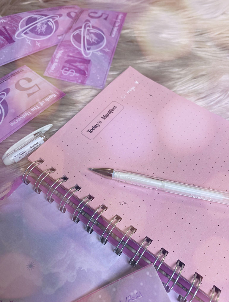 Caderno rosa pontilhado com texto e caneta transparente sobre pelo sintético com cartões rosas ao lado