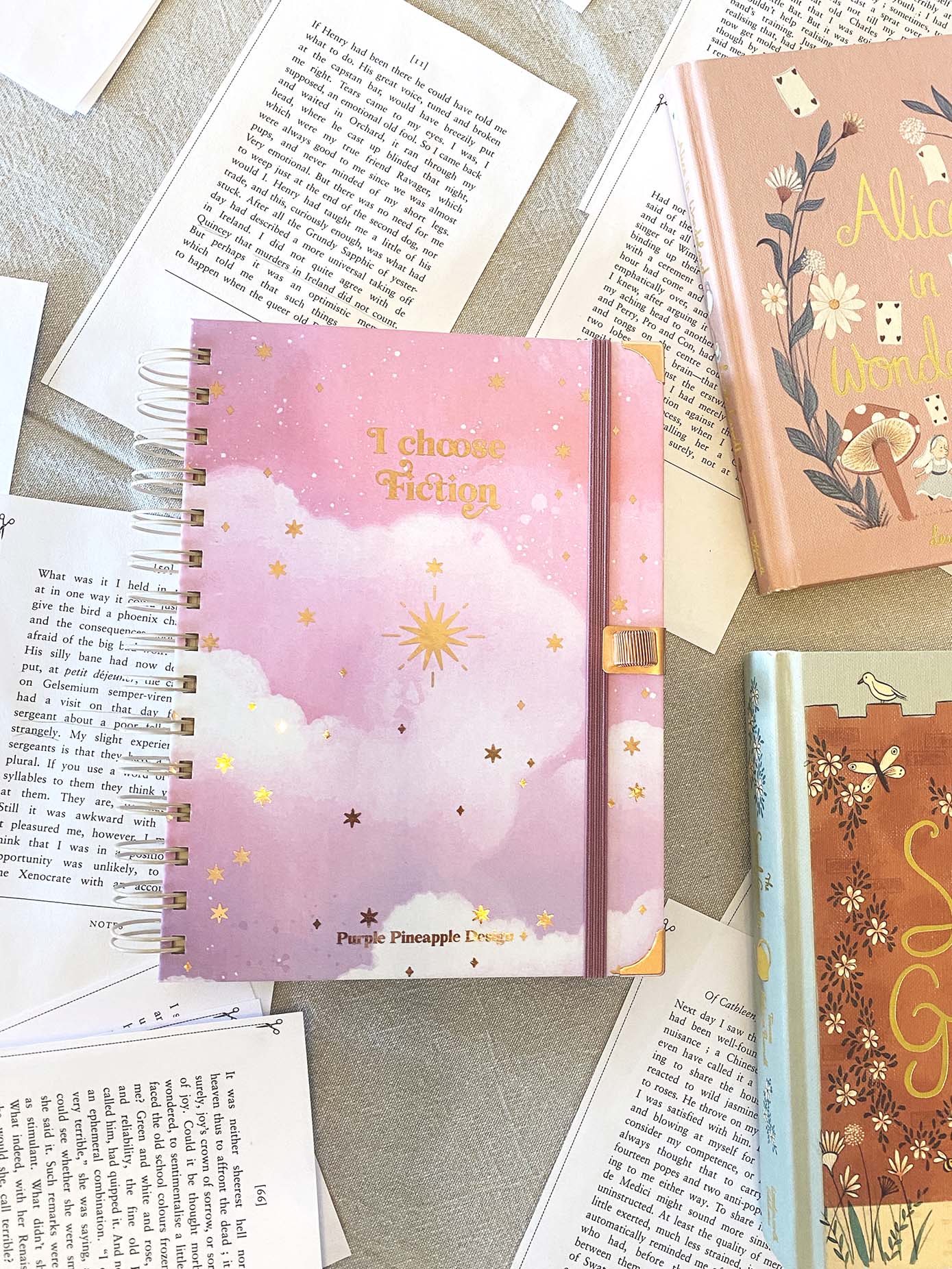 Caderno rosa com estrelas douradas e texto 'I choose Fiction'