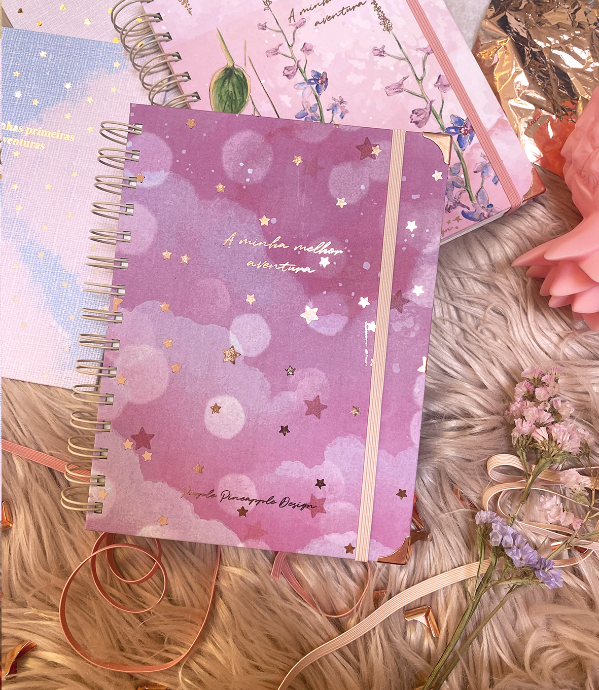 Cadernos coloridos com espiral e padrões de estrelas e bolas sobre superfície peluda com flores e fitas