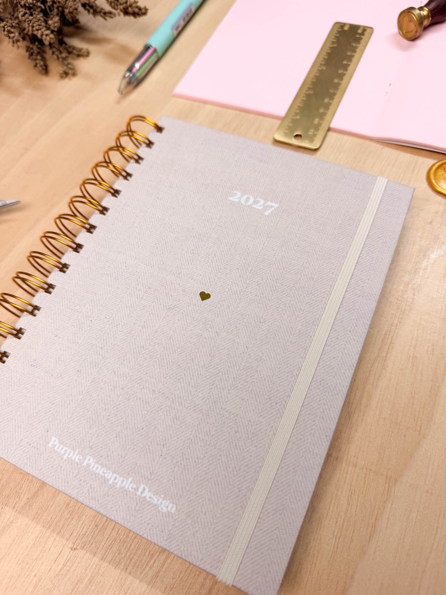Agenda cinza clara com capa de tecido, espiral dourada e texto 2027
