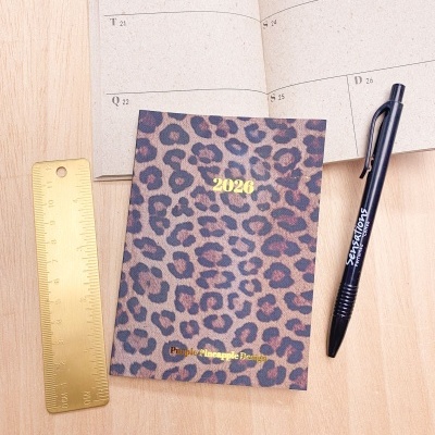 Caderno animal print 2026 com régua dourada e caneta preta sobre mesa de madeira