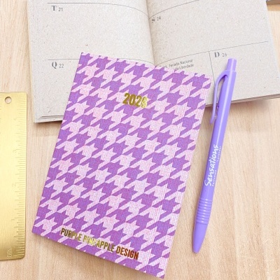 Caderno 2026 com padrão roxo, caneta roxa e régua dourada sobre mesa