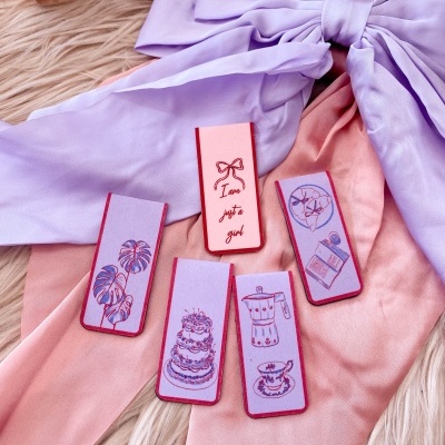 Cinco marcadores de livro decorados em tecido lilás e rosa sobre tecido com laço lilás e fundo felpudo bege