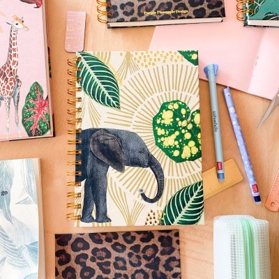 Cadernos espiral com várias capas coloridas e padrões variados sobre mesa de madeira com material escolar