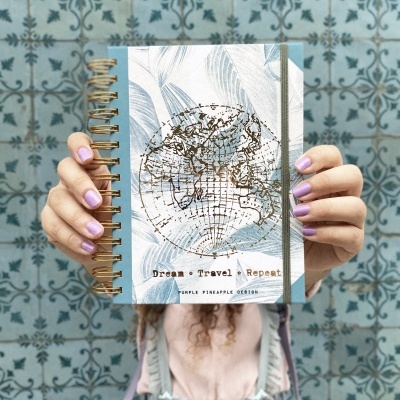 Caderno espiral com capa decorada com mapa e texto, em fundo de azulejos azuis