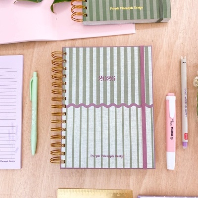 Cadernos riscado verde com canetas e régua numa mesa de madeira