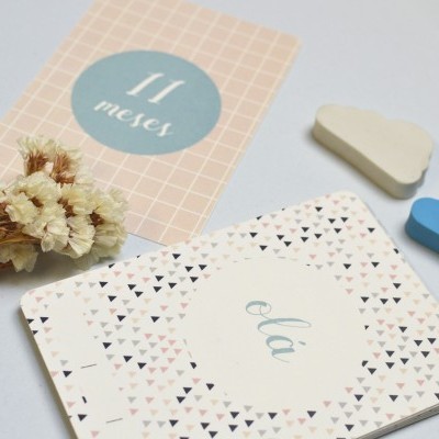 Cartões de marco de bebé com texto em português, flores secas e objetos em forma de nuvem sobre superfície branca.