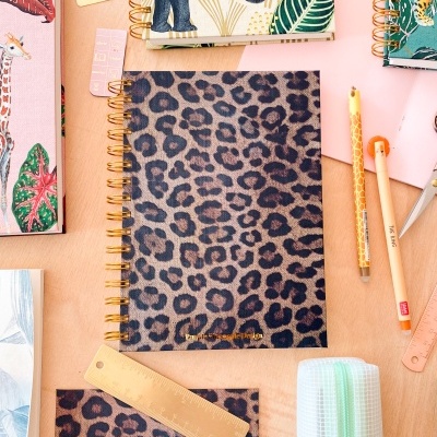 Cadernos espiral com capas de animais e padrões coloridos sobre uma mesa de madeira clara.