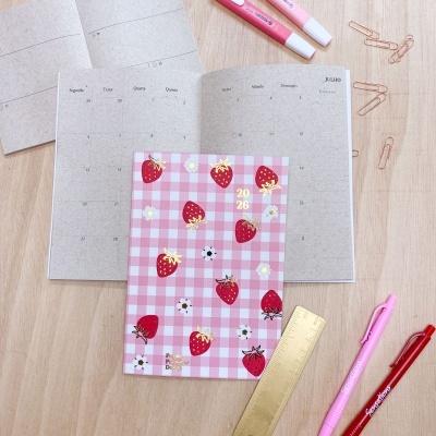 Agenda 2023 rosa com morangos, canetas e clips sobre mesa de madeira