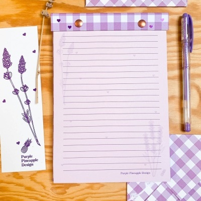 Conjunto de papelaria lilás com bloco de notas, envelope, marcador, caneta e flores secas