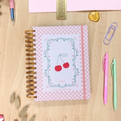 Caderno espiral com capa rosa e branca decorada com cerejas vermelhas e moldura verde