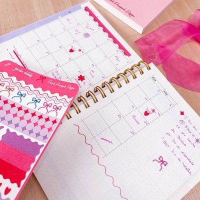 Caderno de organização com autocolantes coloridos e livro rosa com frase motivacional