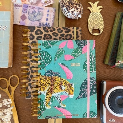 Dois agendas com capas animais e acessórios diversos sobre mesa de madeira