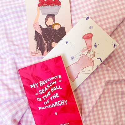 Três postais coloridos sobre tecido xadrez lilás e branco com texto político e ilustrações femininas.