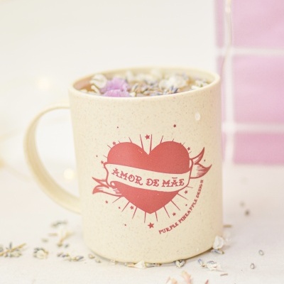 Caneca bege com coração vermelho e frase Amor de Mãe, bebida quente com flores secas encima