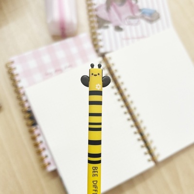 Lápis amarelo e preto com tema de abelha em frente a cadernos espiral com capas rosa e branco