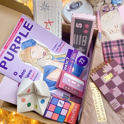 Caixa com artigos de papelaria como revista Purple, bloco de notas xadrez e brinquedo de papel colorido.