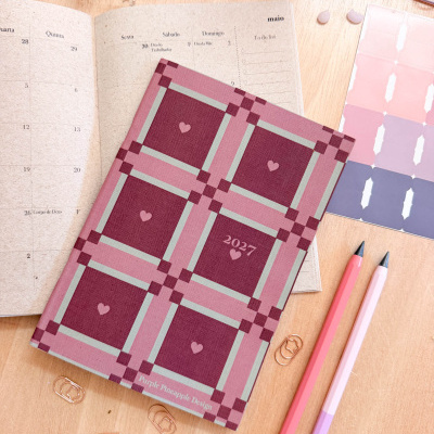 Agenda com padrão quadriculado rosa e vermelho, canetas e clipes em madeira clara