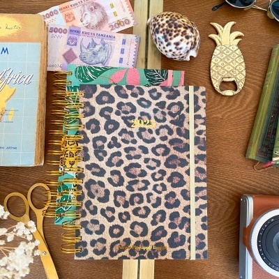Agenda 2022 com padrão leopardo e objetos variados numa mesa de madeira