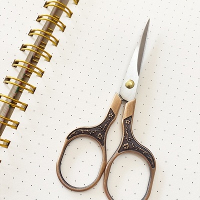 Tesoura pequena com pega em madeira decorada sobre página pontilhada de caderno.