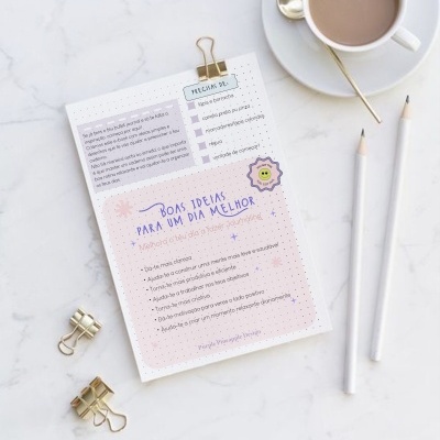 Folha com lista de ideias, clips dourados, lápis e chávena com bebida numa mesa clara.