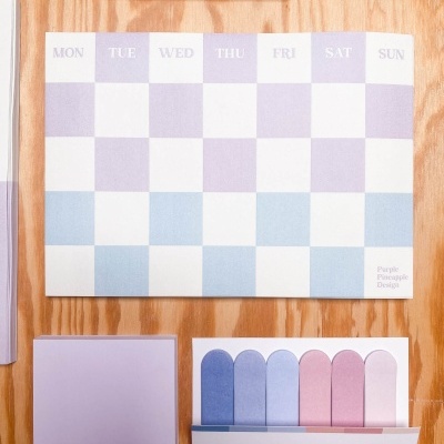 Calendário semanal com marcador e notas autocolantes em tons pastel sobre mesa de madeira